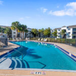 1-BR Apartments in Palm Bay FL - Meri Palm Bay - Gated Pool with Lounge Chairs and Palm Trees.