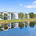 Apartments for Rent in Palm Bay, FL - Meri Palm Bay - Pond Surrounded by Grass and Apartment Building.