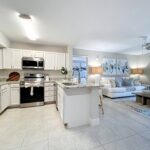 Kitchen with tile flooring, stainless steel appliances, granite countertops, designer lighting, and open access to the living room